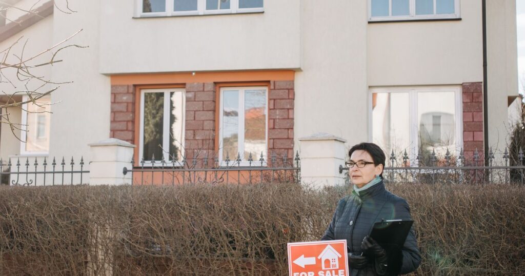 Real estate agent standing by a for sale sign outside a house