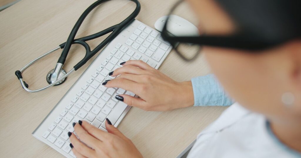 Doctor typing on a computer keyboard with a stethoscope on the desk