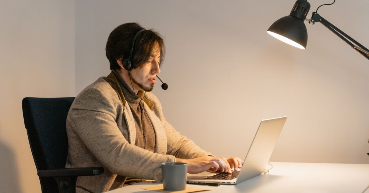 Professional working on a laptop at a desk wearing a headset, in a modern office