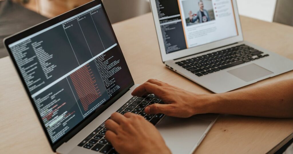 Developer typing code on a laptop while reviewing a second screen